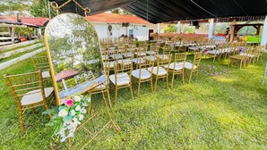 An outdoor wedding setup with rows of chairs under a tent, a floral arrangement, and a sign with names.