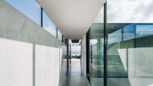 A modern corridor with glass walls and a concrete floor, leading to a distant view. - Triptych - The Blunt House (Tasman)