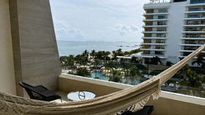 A balcony with a hammock, a small table, and a view of a pool and buildings. - Garza Blanca Cancun 2BR Suite Full Kitchen 
1980 avg. sq. ft.
Max:6 guests (Cancún)