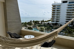 Ein Balkon mit einer Hängematte, einem kleinen Tisch und Blick auf einen Pool und Gebäude.
