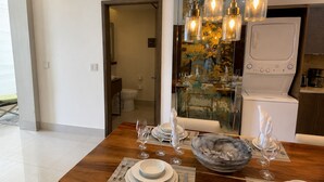 A dining area with a wooden table set for four, a bowl of fruit, and a modern kitchen in the background. - Garza Blanca Cancun 2BR Suite Full Kitchen 
1980 avg. sq. ft.
Max:6 guests (Cancún)