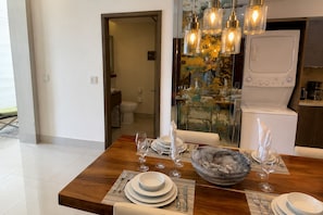 A dining area with a wooden table set for four, a bowl of fruit, and a modern kitchen in the background.