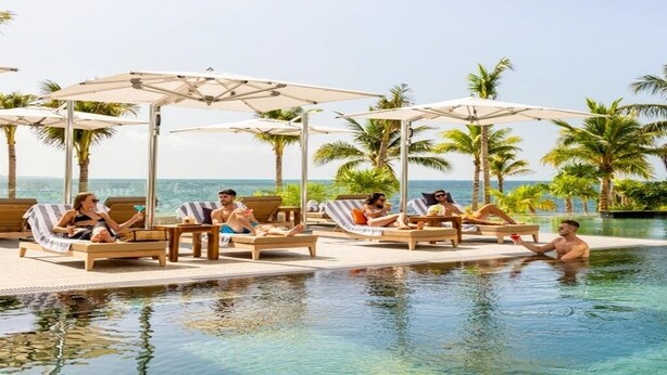 A poolside area with lounge chairs and umbrellas, a clear view of the ocean, and palm trees. - Garza Blanca Cancun 2BR Suite Full Kitchen 
1980 avg. sq. ft.
Max:6 guests (Cancún)