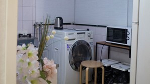 Une cuisine compacte équipée d’un lave-linge, d’un four à micro-ondes et d’un petit tabouret en bois.