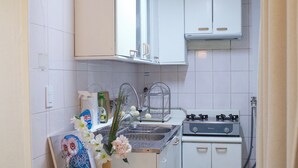Eine kleine Küche mit weißen Schränken, einem Gasherd, einem Spülbecken und einem Tisch mit einem Blumenstrauß.