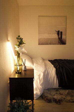A bedroom with a bed, a bedside table with a vase and candles, a picture on the wall, and a fur rug on the floor. - 4min from Hongdae Univ Station/Seoul/4bed/3room (Seoul)