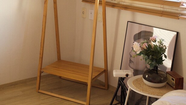Ein Zimmer mit einem Schaukelstuhl aus Holz, einem kleinen Tisch mit Radio und Vase sowie einem Fenster mit Jalousien.