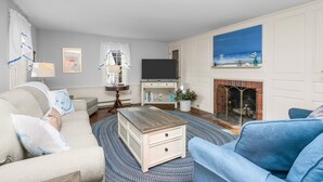 Una sala de estar con chimenea, televisor y un ventanal con cortinas.