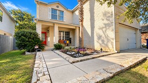 A two-story house with a stone pathway leading to the front door, a garage, and a well-maintained front yard with various plants. - Glampstead Retreat | BMT|SixFlags|SeaWorld|Cantera (San Antonio)