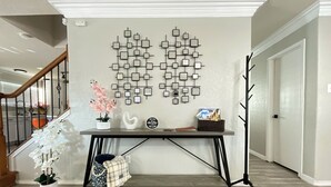Een gang met een aan de muur bevestigd abstract kunstwerk, een console tafel met decoratieve objecten, en een trap op de achtergrond.