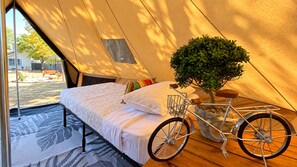 A tented room with a bed, pillows, a small tree, and a bicycle. - Glampstead Retreat | BMT|SixFlags|SeaWorld|Cantera (San Antonio)