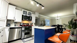 A modern kitchen with stainless steel appliances, white cabinetry, and a central island with seating. - Glampstead Retreat | BMT|SixFlags|SeaWorld|Cantera (San Antonio)