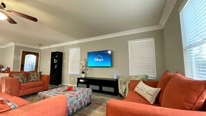 Ein Wohnzimmer mit Fernseher, auf dem das Disney+-Logo zu sehen ist, Deckenventilator und einem Fenster mit Jalousien.