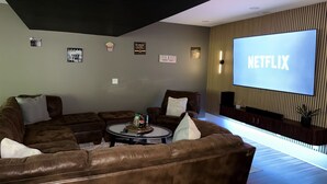A living room with a brown leather couch, a coffee table with snacks, a large screen displaying 'NETFLIX,' and a wall-mounted TV shelf. - Family Retreat -Theater, Games, FREE Platinum Pool Pass (Massanutten)