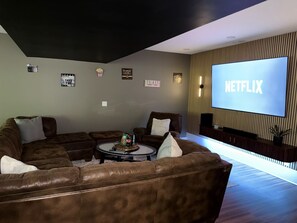 Un salon avec un canapé en cuir marron, une table basse sur laquelle sont posés des en-cas, un grand écran affichant le logo « NETFLIX » et une étagère murale pour la télévision.