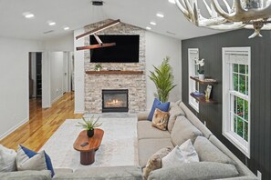 A modern living room with a stone fireplace, a sofa, a coffee table, and a television mounted on the wall. - 3BR + Bonus Room Theater • Game Room • Mountain Retreat (Massanutten)