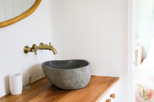 Une salle de bain avec un lavabo en pierre, un robinet en laiton, un plan de toilette en bois et un miroir.