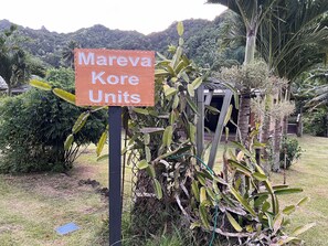 A sign for 'Mareva Kore Units' in a lush garden setting with tropical plants and a mountainous backdrop. - Mareva Kore Unit 1 (Avarua)