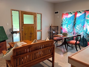 A room with a wooden door, a fan, a table with chairs, and a colorful curtain. - Mareva Kore Unit 1 (Avarua)