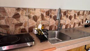 A kitchen with a stone backsplash, stainless steel sink, and a black induction cooktop. - Mareva Kore Unit 1 (Avarua)