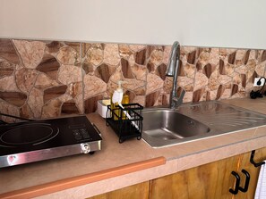 A kitchen with a stone backsplash, stainless steel sink, and a black induction cooktop. - Mareva Kore Unit 1 (Avarua)