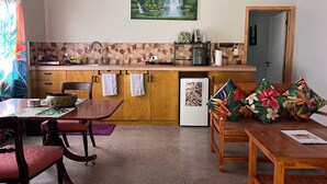A compact kitchen with a stone backsplash, wooden cabinets, a sink, and a refrigerator. - Mareva Kore Unit 1 (Avarua)