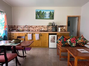 A compact kitchen with a stone backsplash, wooden cabinets, a sink, and a refrigerator. - Mareva Kore Unit 1 (Avarua)