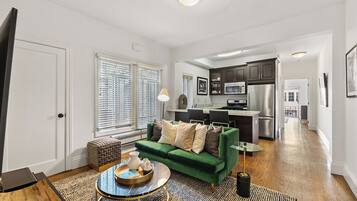 A modern living room with a green sofa, a coffee table, and a dining area with a glass table.