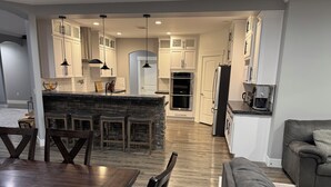 A modern kitchen with white cabinets, a central island with stools, a dining table with chairs, and a gray sofa in the living area. - Peaceful 4-bedroom house near lake access with room for multiple boats. (Moses Lake)
