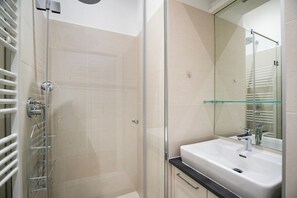 Une salle de bain moderne avec une douche à l’italienne en verre, un lavabo blanc et une étagère en verre.
