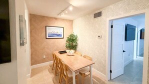 Ein Essbereich mit einem Holztisch, Stühlen, einer Topfpflanze und einem gerahmten Bild an der Wand.