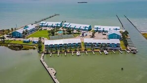 An aerial view of a coastal hotel with multiple buildings, a dock, and a pier extending into the water. - Beachfront Water View in Perfect Paradise at Bayfront Kontiki! (Rockport)