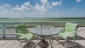 A deck with a round table and two chairs, overlooking a calm sea and a pier in the distance. - Beachfront Water View in Perfect Paradise at Bayfront Kontiki! (Rockport)