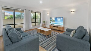 Uma sala de estar moderna com sofás cinza, uma mesa de centro e uma TV sobre um suporte de madeira.
