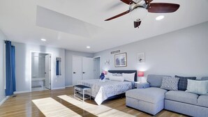 Ein geräumiges Schlafzimmer mit einem großen Bett, einer Couch, einem Deckenventilator und Blick auf das Badezimmer.