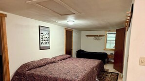 Un dormitorio con una cama grande, una cama más pequeña, una puerta de madera, un perchero y un cartel en la pared.