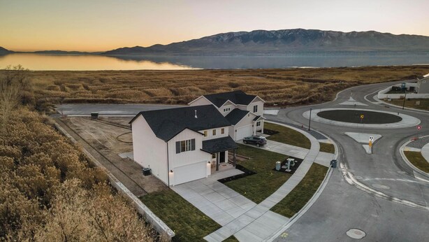 Una casa moderna con entrada de vehículos y una glorieta, rodeada de paisaje natural y montañas.