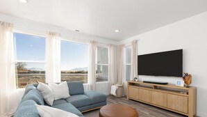 Una sala de estar moderna con un ventanal grande, un sofá gris, un mueble bajo de televisión de madera y un televisor de pantalla plana.