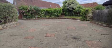 A courtyard with stone paving, a brick building, and lush greenery.