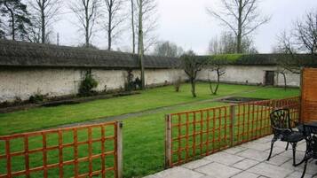 A courtyard with a thatched-roof building, a paved pathway, and a fenced area with chairs.
