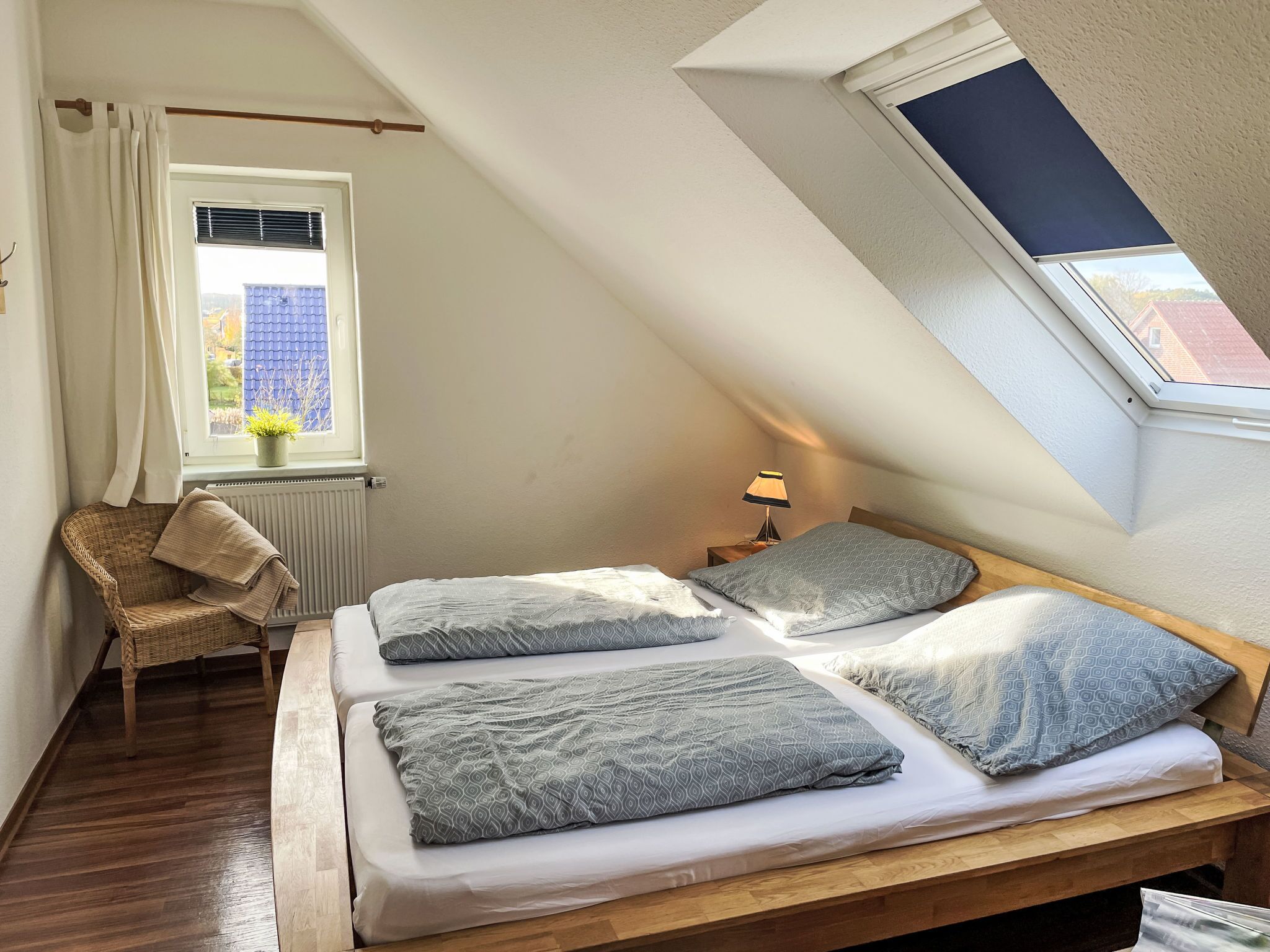 A cozy attic bedroom with a sloped ceiling, a wooden bed frame, and a window with a view of buildings outside.