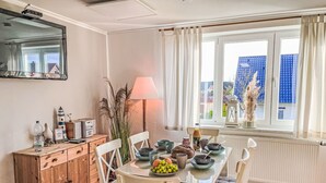 Een eetgedeelte met een tafel voor vier personen, een houten kast, een lamp en een uitzicht op gebouwen door een raam.
