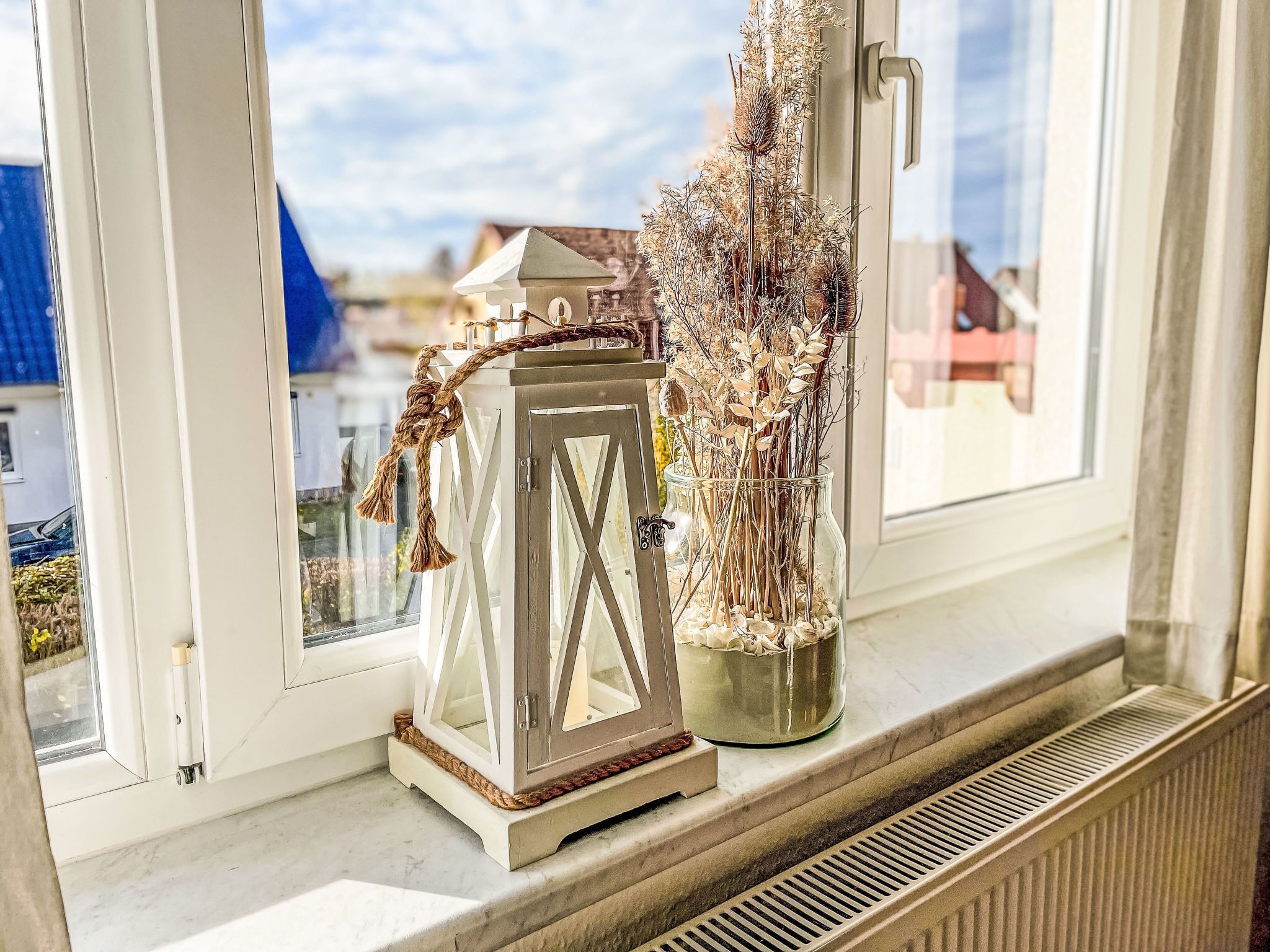A window sill with a white lantern and a vase of dried plants.