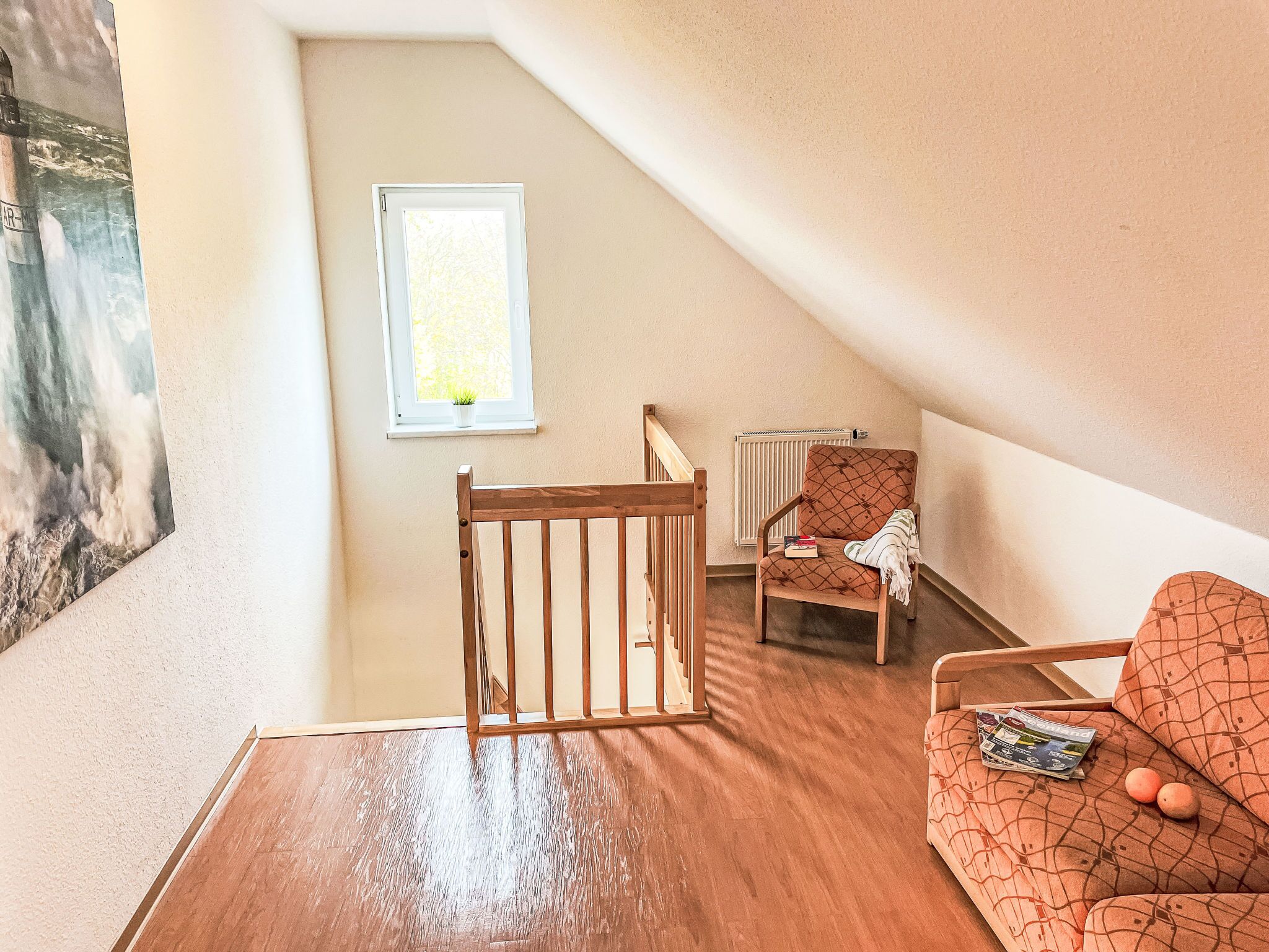 A cozy attic room with a wooden crib, a cushioned chair, and a sofa with magazines and a plush toy.