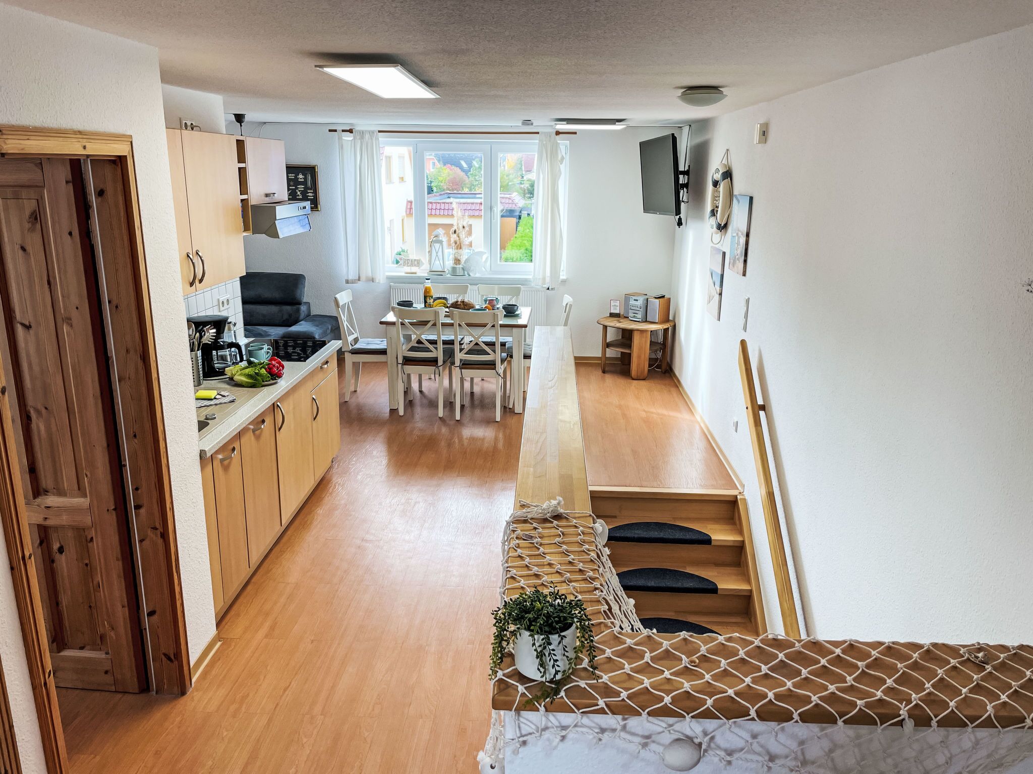 A modern kitchen with wooden cabinets, a dining area with a table and chairs, and a staircase leading to a second floor.