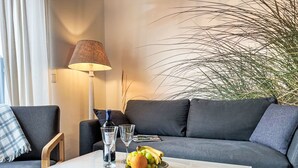 En moderne stue med en grå sofa, et hvidt sofabord, en lampe og en potteplante.