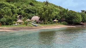 Ein tropisches Resort mit strohgedeckten Hütten, einem Boot und üppiger Vegetation entlang eines Flussufers.