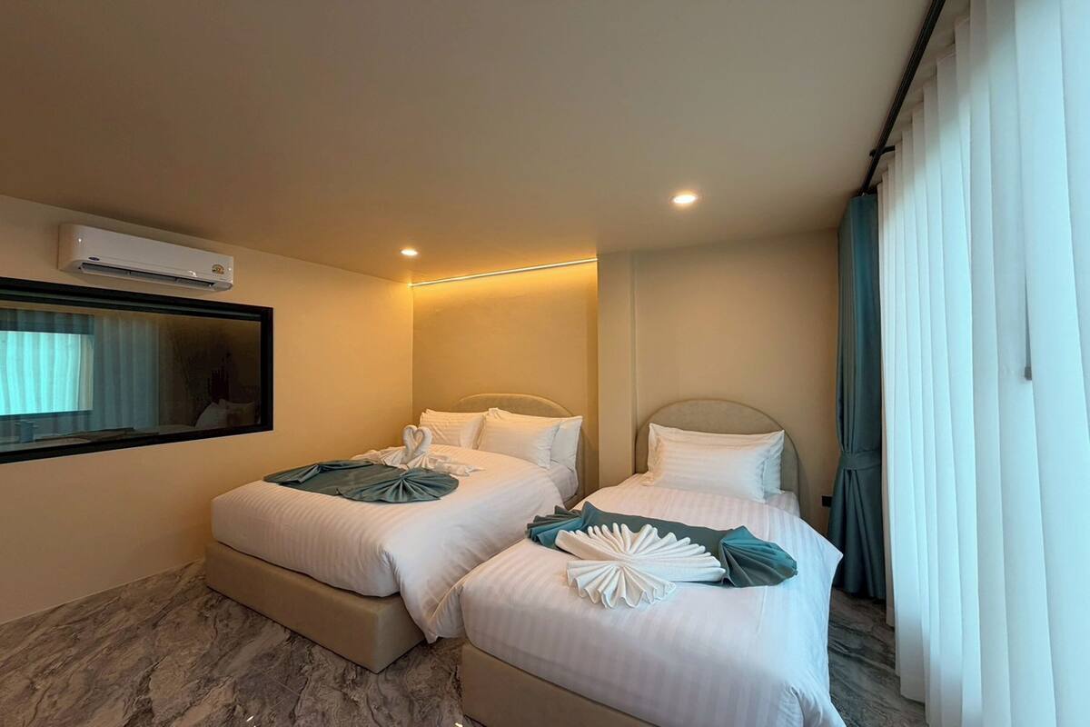Une chambre d’hôtel avec deux lits, un grand miroir, un appareil de climatisation et une fenêtre avec des rideaux.
