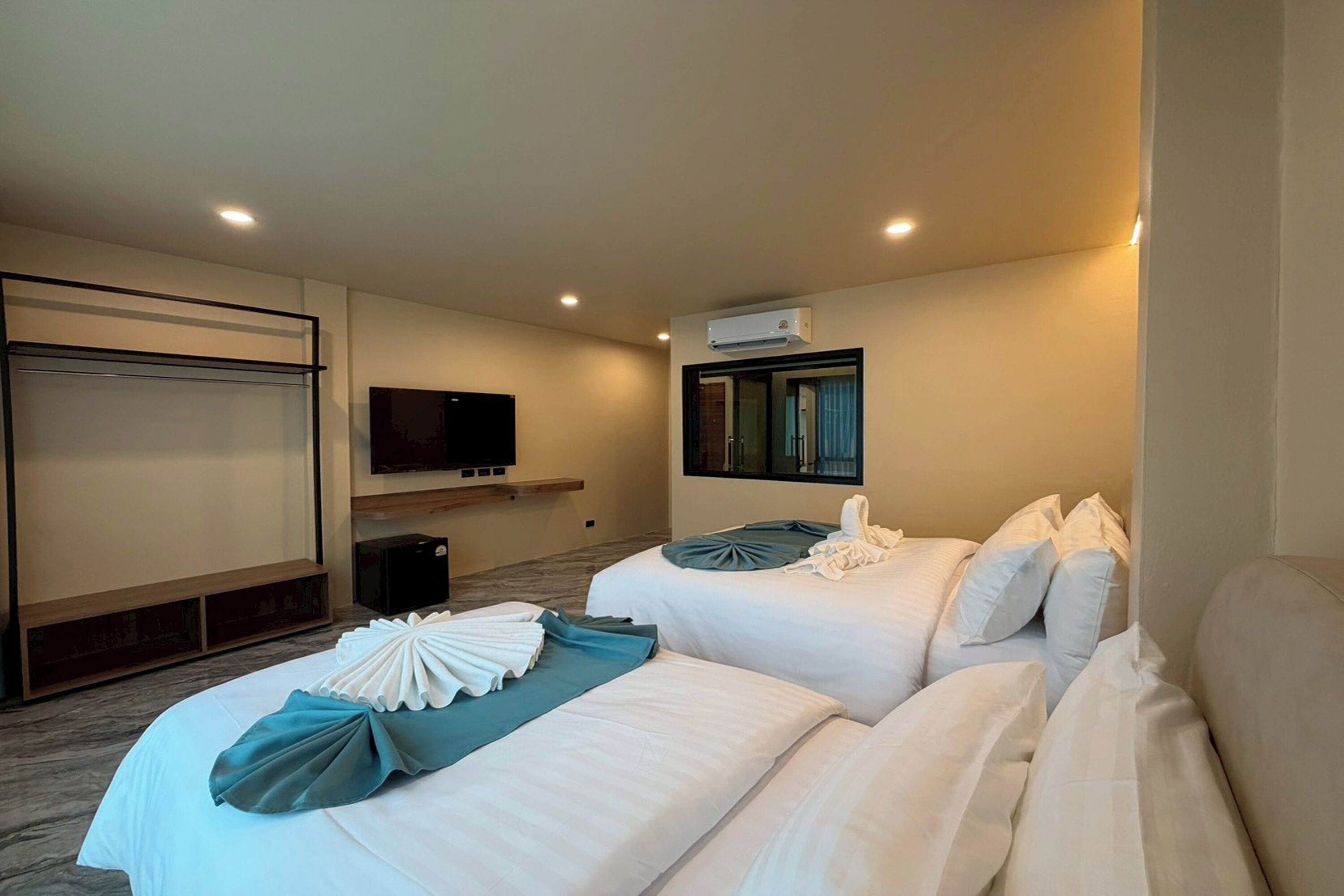 A hotel room with two beds, a flat-screen TV, an air conditioning unit, and a small seating area with a bench.