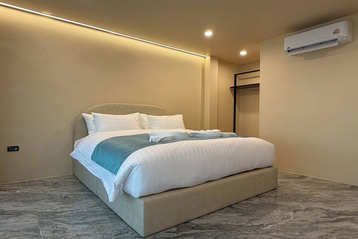 Une chambre à coucher moderne avec un grand lit, une table de chevet et un climatiseur fixé au mur.
